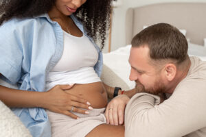 Smiling man looks at his wife's belly as they discuss their IVF options | Reproductive Science Center of the SF Bay Area